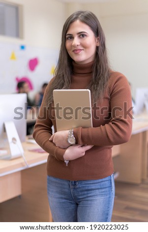 Portrait of a pretty cheerful casual turkish girl holding tablet or ipad inside modern computerlab classroom. Technology and education concept