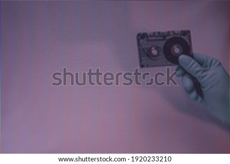 Green Hand holding audio cassette tape in the color light. Beautiful minimal in neon light. Minimalism retro style concept.  Macro  photography view. Close-up of pixel.