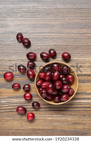 Top view of ripe red cranberries in a small wooden bowl and on wooden table top