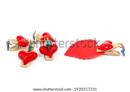 selective focus of miniature workers holding red heart shape wood clip isolated on white background