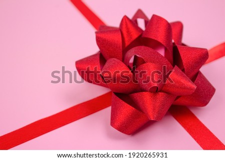 Close up view of composition with decorative red ribbon bow on pink background with copy space for text. Giving presents, holidays sale or giveaway concept. Greeting card design. Selective focus