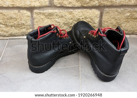 Black walking boots with red laces awaiting cleaning on grey tiled floor with stone coloured bricks to the rear, after a day walking in the great outdoors. Lancashire Pennine hiking.