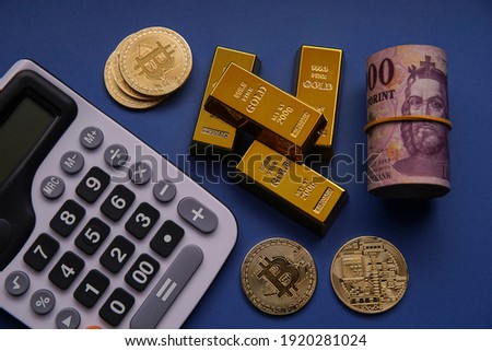 Tools, calculator, gold bars, bitcoun and a 1000 forint roll on the blue table. Bank image and photo. 