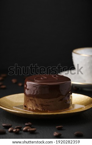 Austrian cake, sackertorte. Chocolate cake on a golden plate. Coffee beans on a black textured table. White cup with cappuccino. Side view of a chocolate dessert.
