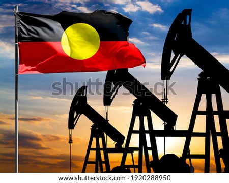 Oil rigs against the backdrop of the colorful sky and a flagpole with the flag of Australian Aboriginal. The concept of oil production, minerals, development of new deposits.