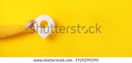 3D location symbol in hand over yellow background, panoramic image Royalty-Free Stock Photo #1920290390