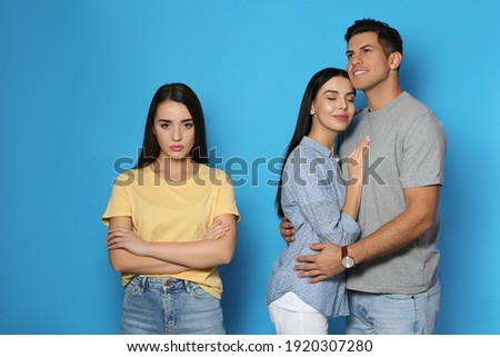 Unhappy woman feeling jealous while couple spending time together on blue background