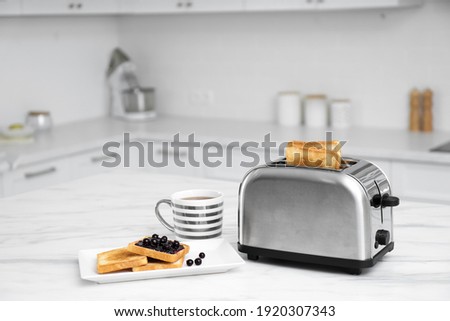 Modern toaster and tasty breakfast on white marble table in kitchen