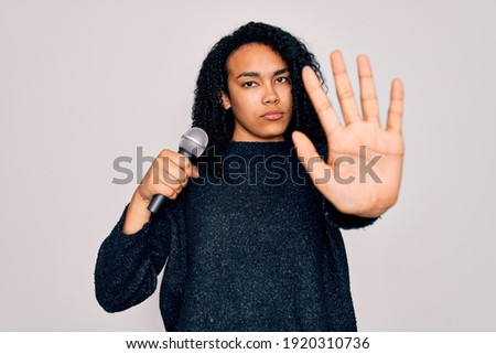 Young african american curly singer woman singing using microphone over white background with open hand doing stop sign with serious and confident expression, defense gesture