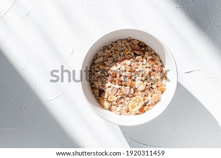 Delicious healthy breakfasts muesli with raw oatmeal, dried fruits and nuts on white background in sunny morning with light. Vegan food, top view
