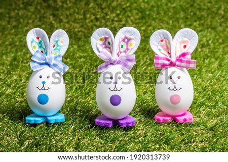Traditional Easter festive concept. Multicolored cute handmade rabbits from eggs on green grass background, copy space