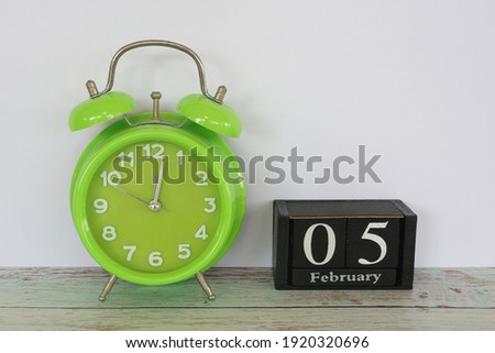 green alarm clock and cube calendar date February 5 on the table