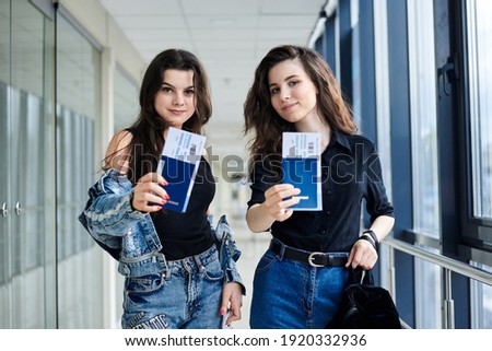 Close-up picture of two young brunette girls, holding international passports and boarding passes tickets in light airport hallway, waiting for document control. Friends traveling by air.