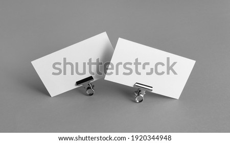 Two blank business cards and metal binder clips on gray background.