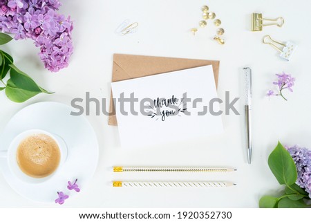 Flat lay top view home office workspace - blank card with lilac flowers on white background