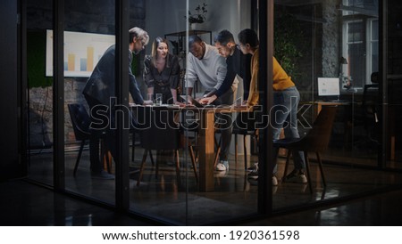Young Creative Team Meeting with Business Partners in Conference Room Behind Glass Walls in Agency. Colleagues Sit Behind Conference Table and Discuss Business Opportunities, Growth and Development.