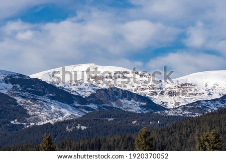 Beautiful winter panoramic natural mountain landscape. Attractive snowy peaks of Rila Mountains, Bulgaria. White clouds in dynamic blue sky, perfect conditions for tourism recreation and winter sports