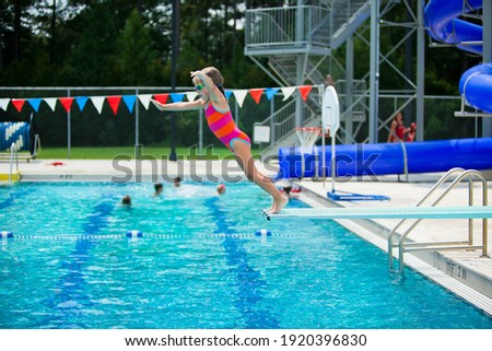 Little girl jumping off the diving board during her swim lessons at the local outdoor pool in the summer Royalty-Free Stock Photo #1920396830