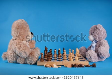 Close up of teddy bears with chess pieces on chessboard. Soft plush toys playing chess on blue background