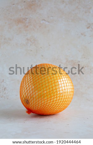 A delicious single yellow pomelo wrapped in a net and plastic foil on neutral background, vertical with copy space