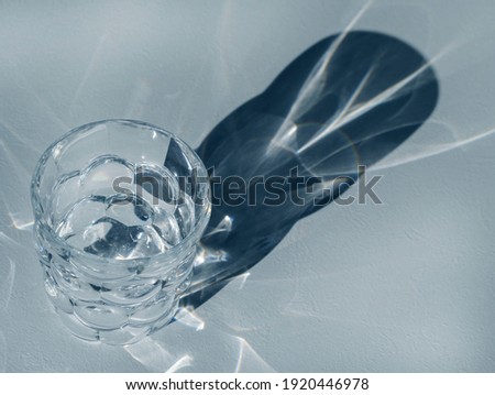  Empty glass on light grained background with hard shadows and sun glare. The reflection of the light of the glass. Abstract background.                             