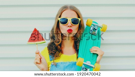 Portrait of young woman with skateboard and ice cream shaped slice of watermelon on a white background