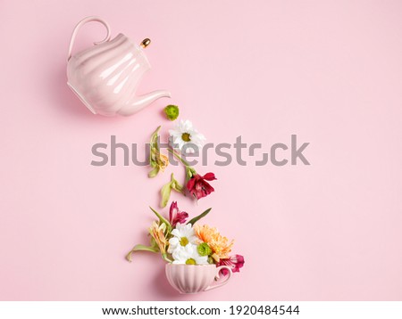 Creative layout with tea pot pouring fresh flowers and leaves into tea cup on pastel pink background. Creative floral spring bloom concept. Still life visual trend. Flat lay. Royalty-Free Stock Photo #1920484544