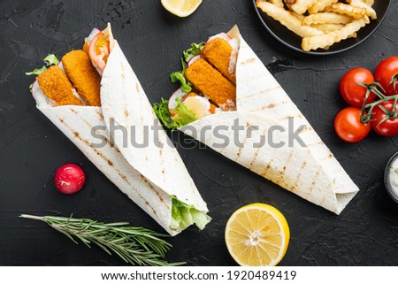 Tortilla roll with fish fingers, cheese and vegetables set, on black background, top view flat lay
