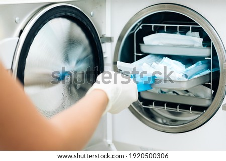 Nurse putting instruments in special craft paper bags into autoclave for processing. Modern laboratory equipment. Tools sterilization, bacterial purification and disinfection in dental clinic. Royalty-Free Stock Photo #1920500306