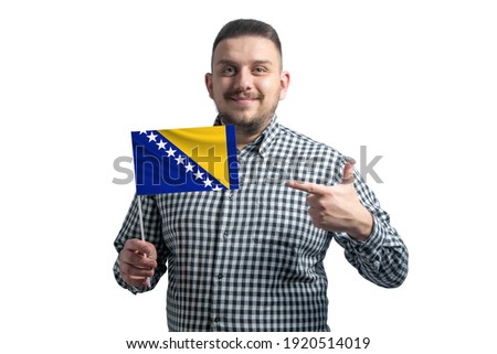 White guy holding a flag of Bosnia and Herzegovina and points the finger of the other hand at the flag isolated on a white background.