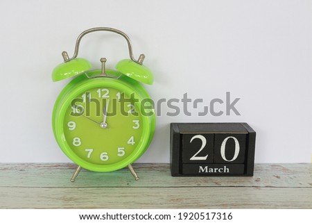 green alarm clock and cube calendar date March 20 on the table