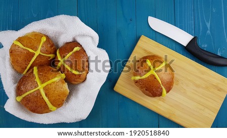 cross buns on a plate. there is a wooden board and a knife nearby. easter pastries. space for the text.