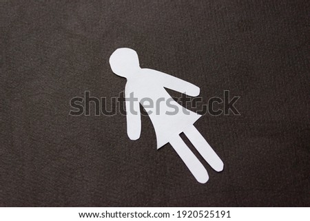 Silhouette of a woman in dress of white paper, cut by hand. In the center of photo on black background