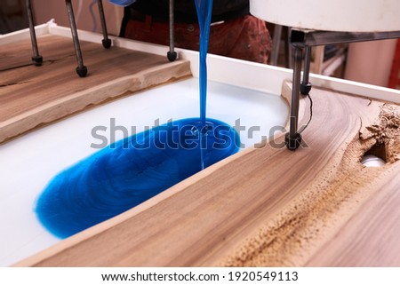 Process making of a craft resin and wood table. Liquid epoxy is poured into a mold with wooden blanks. closeup Royalty-Free Stock Photo #1920549113