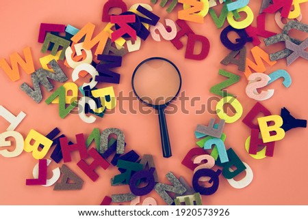 Magnifying glass with colorful alphabet on pink black background.Education concept.
