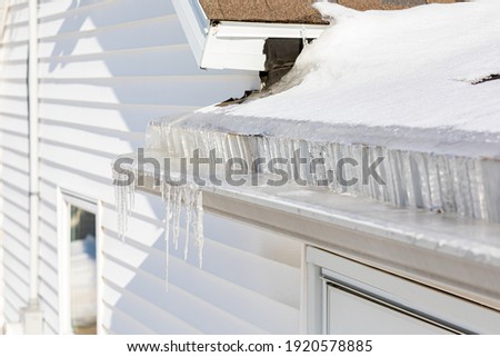 Roof gutter full of ice and icicles after winter storm. Concept of roof damage, home maintenance and repair. Royalty-Free Stock Photo #1920578885