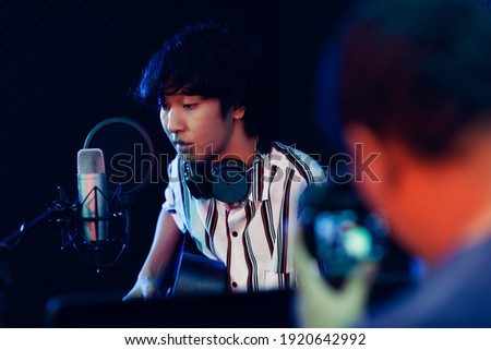 Young and cute teen boy playing guitar in rocording room studio and videographer recording him