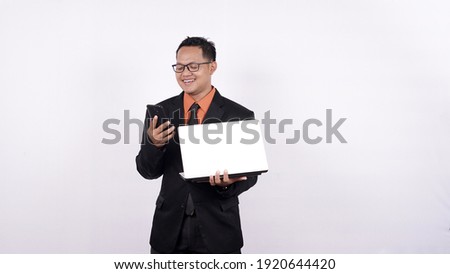 businessman holds a laptop computer and looks at a cell phone isolated white background
