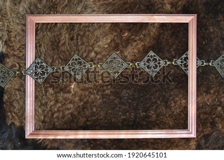 Dark shabby sheepskin fur. Metal decorative belt and photo frame with space for text, artwork, lettering on a fur background. Flat lay, top view. 