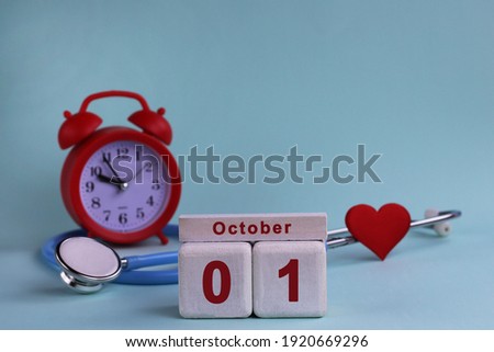 October 1. Day 1st of month, calendar date. White wooden calendar blocks with date, clock and stethoscope on blue pastel background. Selective focus. health concept