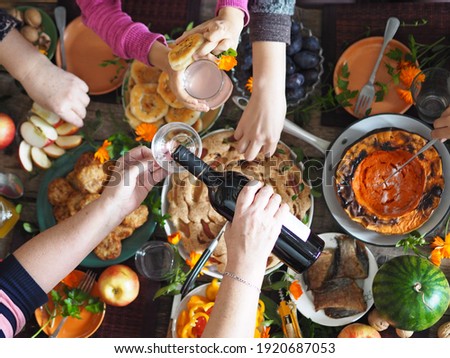 Thanksgiving day celebration concept. There is a lot of food on the wooden table. Guests pour red wine and take healthy homemade natural food with their hands. Royalty-Free Stock Photo #1920687053