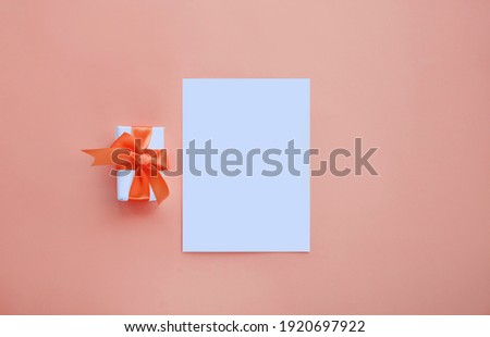 White invitation card mockup with small present box on peach background