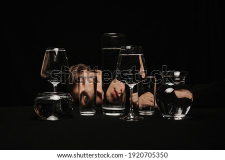 surreal portrait of a man looking through glasses of water on a black background