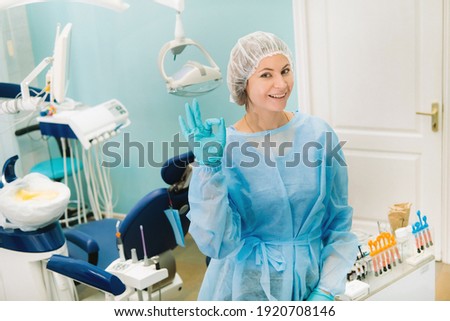 the dentist stands in his office and shows the OK sign