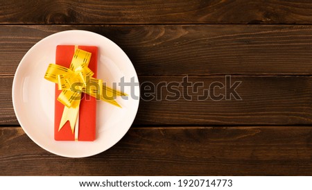 gift in a red box with a yellow bow and a white postcard note on a wooden background. gift in a white plate