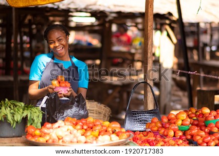 happy nigerian trader in a local market holding a bowl of tomatoes Royalty-Free Stock Photo #1920717383
