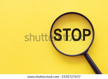 The word STOP is written on a magnifying glass on a yellow background.