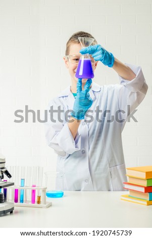 A schoolboy studies multi-colored substances in test tubes, conducts experiments - a portrait on a white background. Concept for the study of coronavirus in the laboratory
