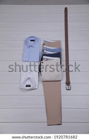 Beige trousers, blue and white shirt and leather belt. Overhead view of men's casual clothes on white wooden background. Lie flat, top view.