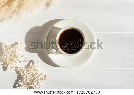 Espresso in a white cup on the table in bright sunlight. Creative composition with dried flowers. Modern breakfast. The concept of freshness of a summer morning. Minimalism, top view